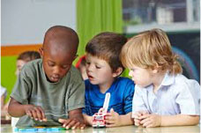 Several young boys lean over a table looking at a book