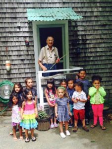 young children of various ethnicities gathered outside a shingled house