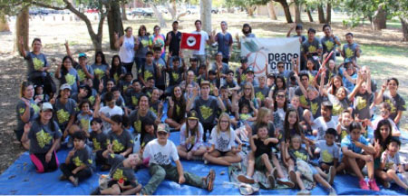 Young children lined up under a tree holding up a peace sign