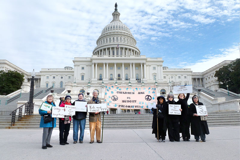 P.E.A.C.E. members protesting in front of the US Capitol building. They hold signs and are waving a banner.