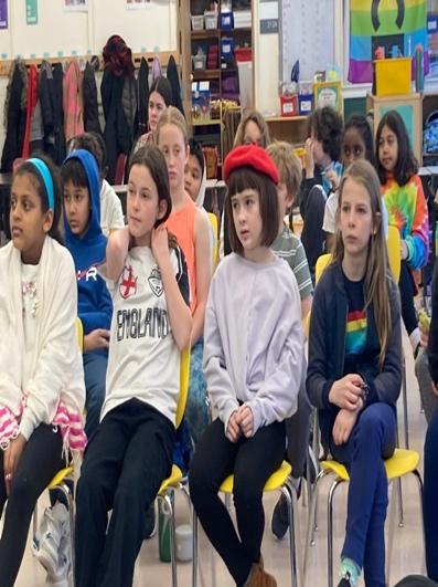 Children seated in rows of yellow plastic chairs in a classroom.