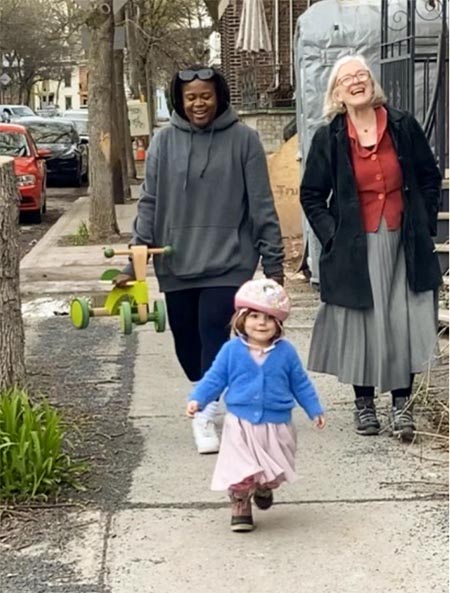 Two women and a young girl walk down a sidewalk in cool weather.