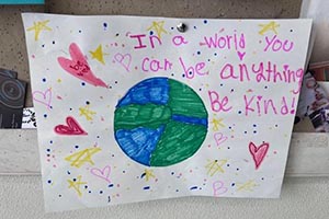 Colorful poster by a child which reads, In a world you can be anything. Be kind!