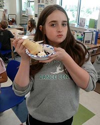 A school-aged child mugs for the camera while holding up their lunch plate.