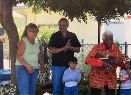 Pam Boneville, Tom Chiaramonte, and Ella Jenkins perform outside with young children singing along.