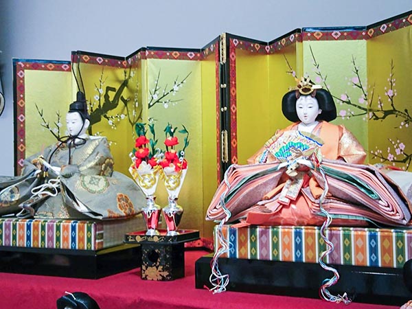 Japanese dolls on platforms in front of a gold screen.
