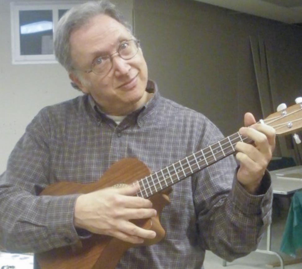 A middle-aged man strumming a small guitar