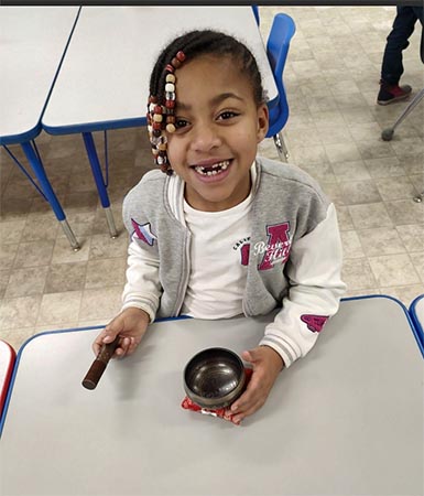 Young girl in braids sitting at a classroom table with a Tibetan singing bowl