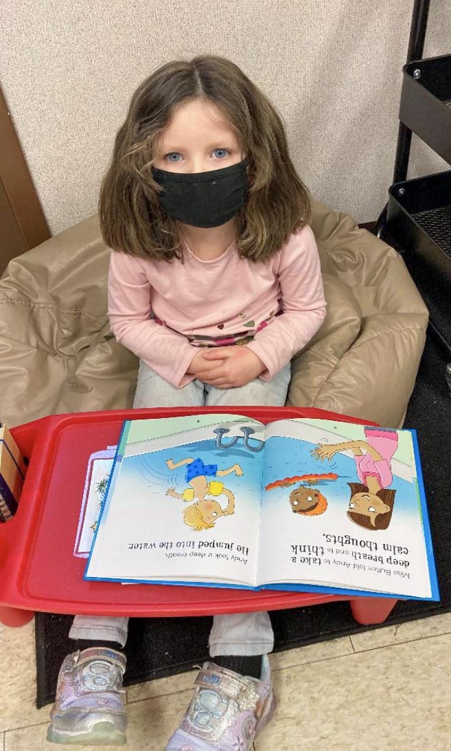 A white preschool-aged girl reads a book in a child-sized chair