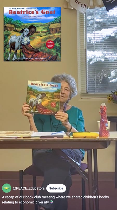 A screen capture of a YouTube social post showing an older woman seated at a school table holding up a children's book.