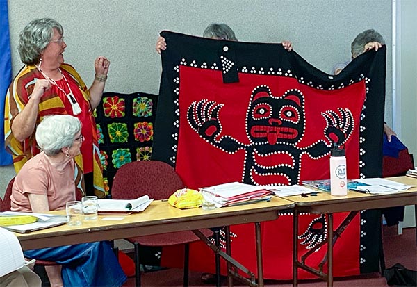 A woman holds up a Native American button blanket with a raven figure created into it