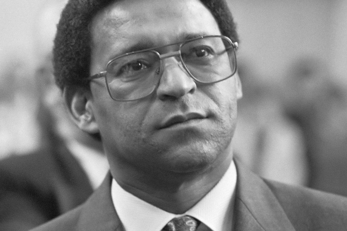 A 1986 black-and-white portrait of Reverend Allan Boesak, a Black man with short dark hair, wearing a suit, tie, and wire-rimmed glasses. Photo by Rob Croes for Anefro, National Archive.