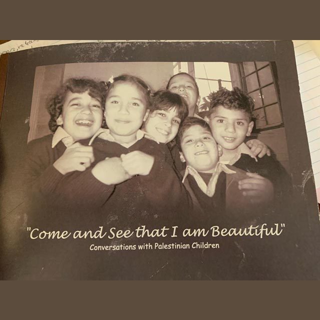 Sepia-toned picture of 6 Palestinian children in their school uniforms laughing and smiling at the camera in a group hug