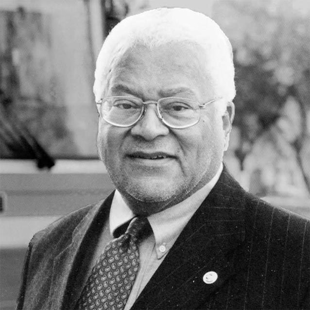 Black-and-white headshot of an older gentleman with white hair and glasses, wearing a suit and tie