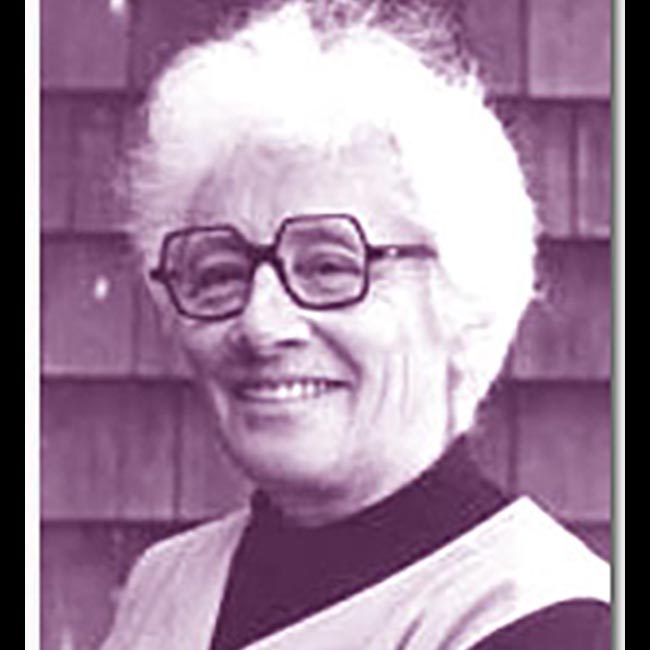 Headshot of Malvina Reynolds. She has short white hair and wears black-framed glasses and a dark turtleneck with a smock on top.