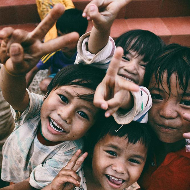 A group of young Vietnamese children smile and look up at the camera, holding their fingers in a 