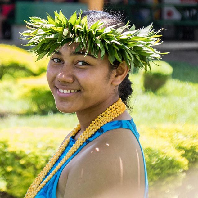 Pacific Islander woman with traditional leaf crown, shell necklace and blue, sleeveless top.