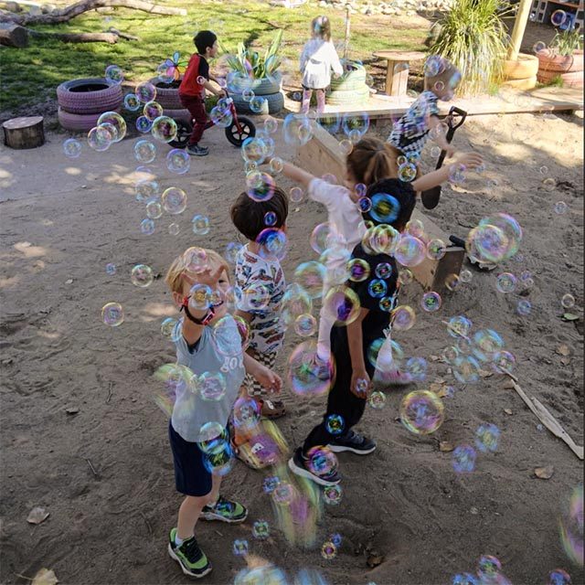 Young children outside blowing bubbles.