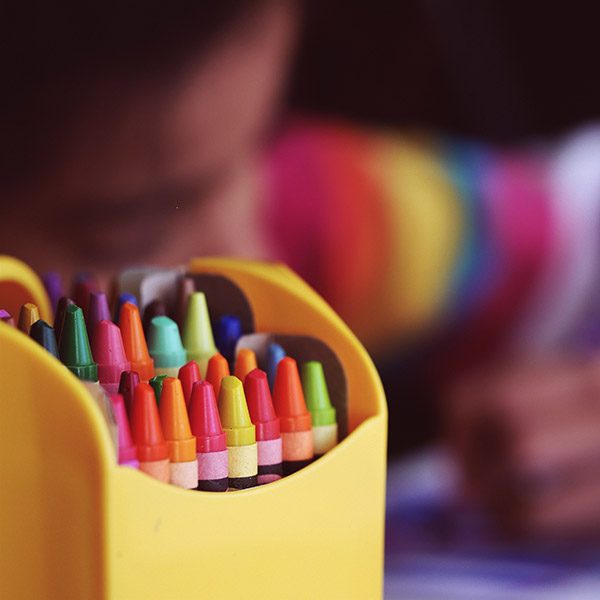 Close up of a box of crayons with a child soft-focus in the background
