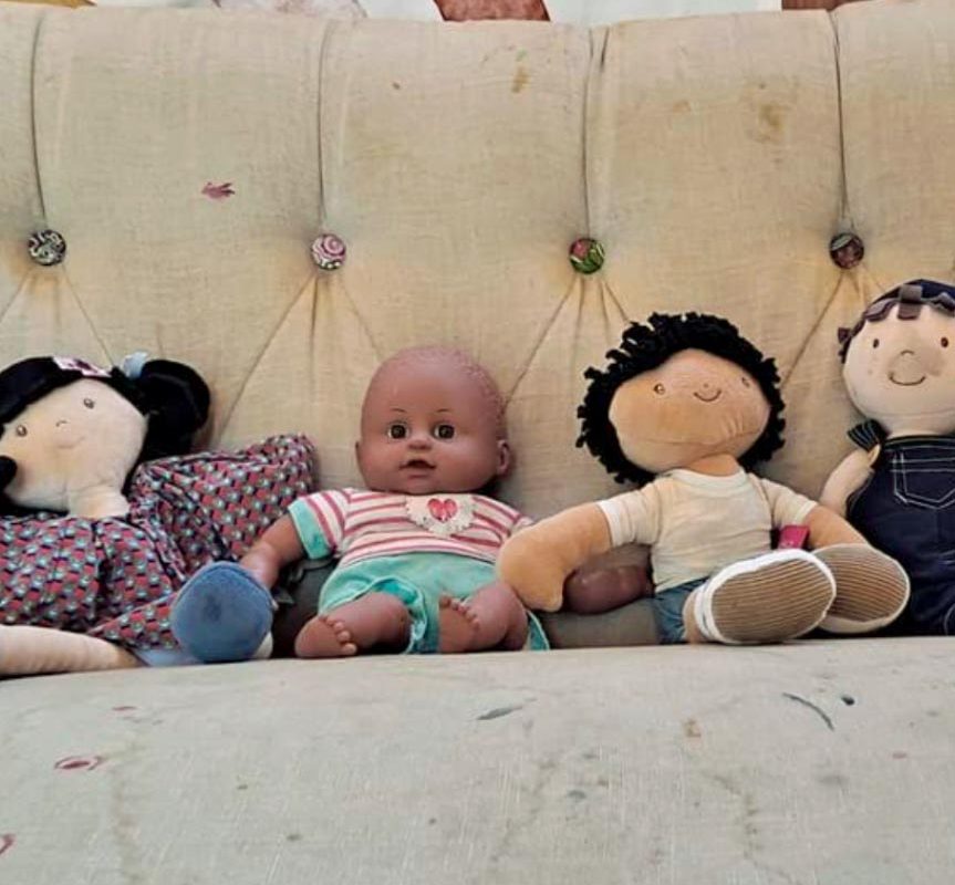 A row of dolls lined up against the back of a sofa.