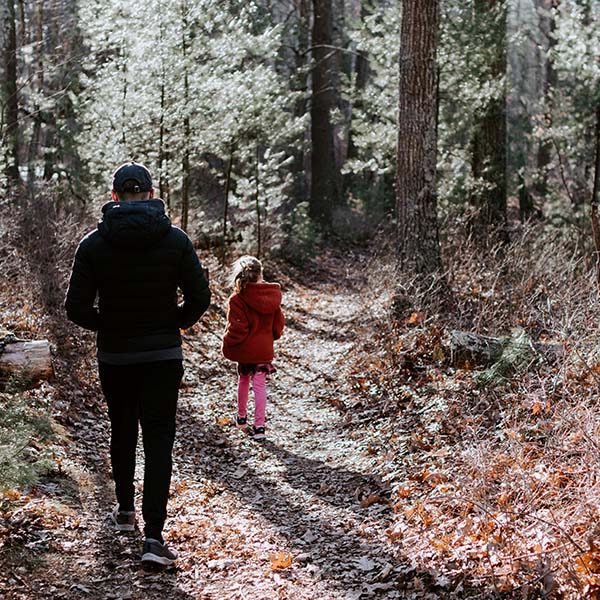 A man and his school-aged daughter hike along a forest trail