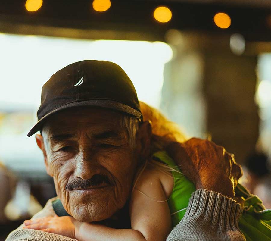 A grandfather in a baseball cap hugs a young girl to him. Her head is behind his and she drapes over his shoulder.
