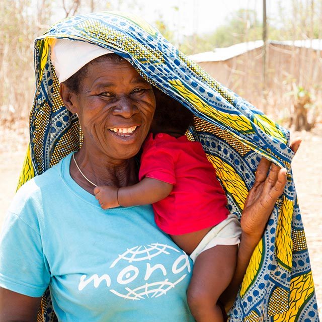 An indigenous woman holding a child in her arms. She protects them both from the sun with a colorful sari.