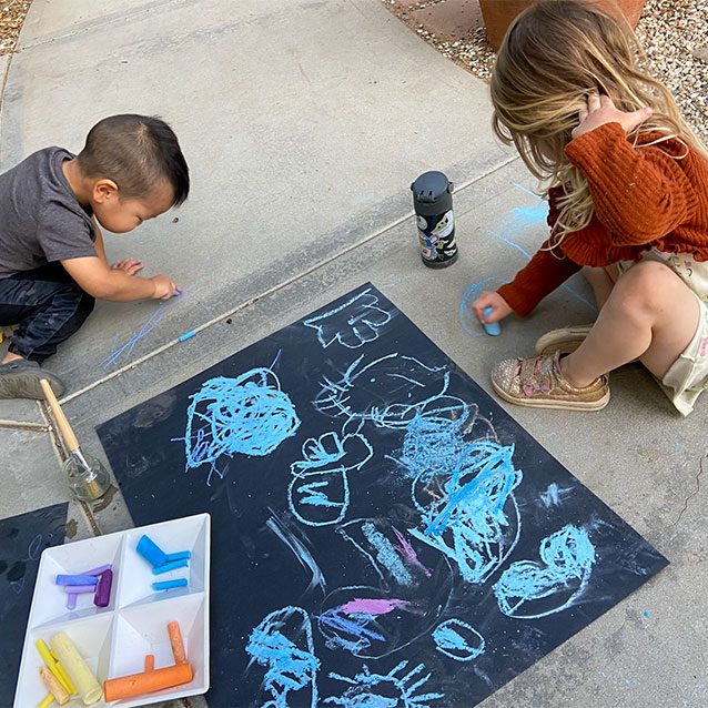 Children seated on the ground concentrating on their chalk drawings.