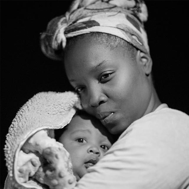 Black-and-white image of a black woman cuddling an infant.