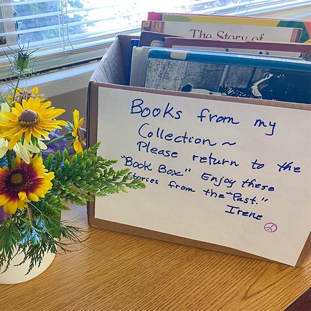 Cardboard box on a desk with childrens books inside. A handwritten note is taped to the front which reads, 