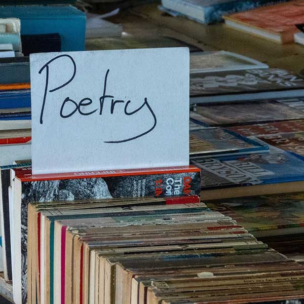Books laying spine-up on a sale table. A hand-written Poetry sign sits on one