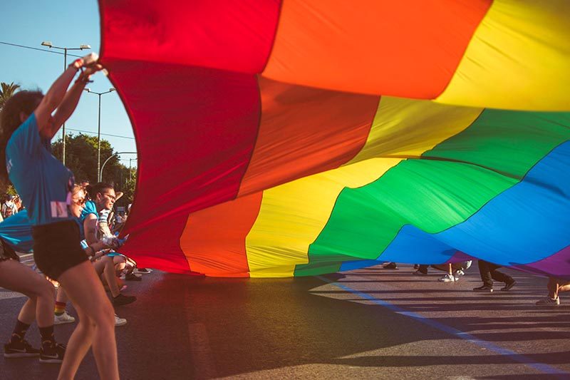 Group of people carrying a huge rainbow flag over the street