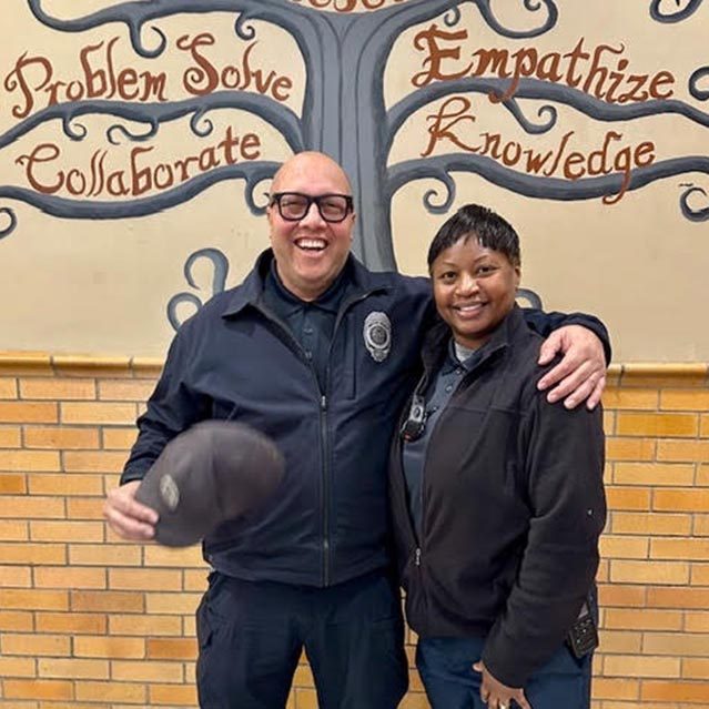 Two security guards pose in front of an inspirational mural with the words, 