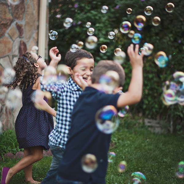 3 children playing in soap bubbles on the lawn