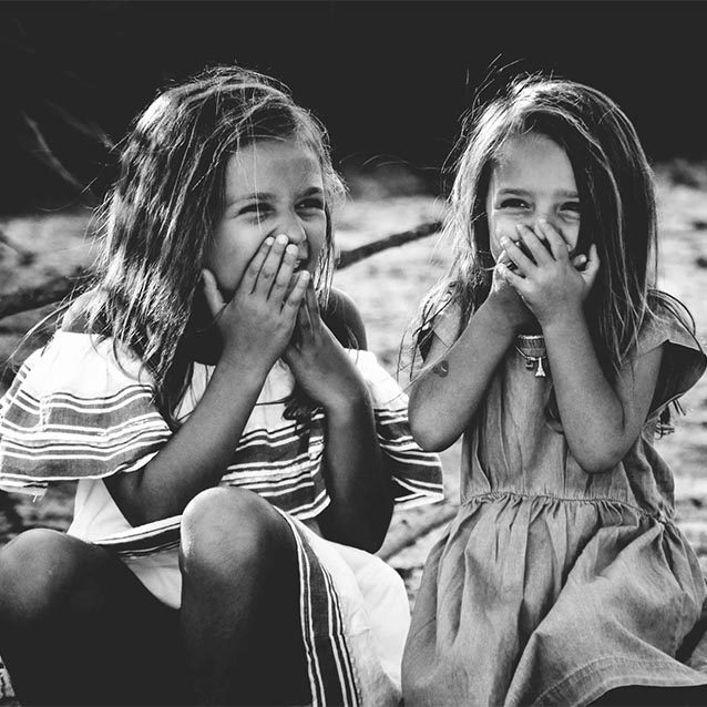 A sepia-toned photo of twin girls in dresses, around 5 years of age