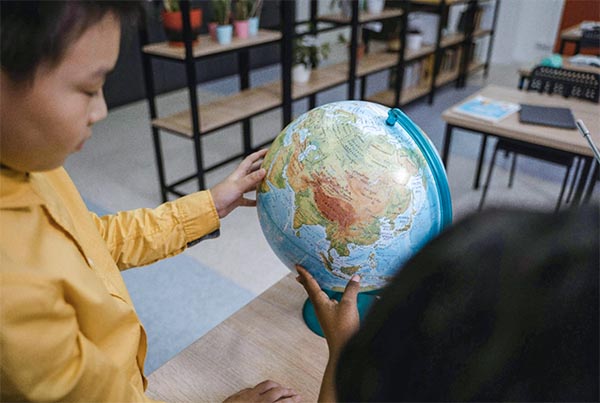 Young child in a classroom reaching out to touch a globe.