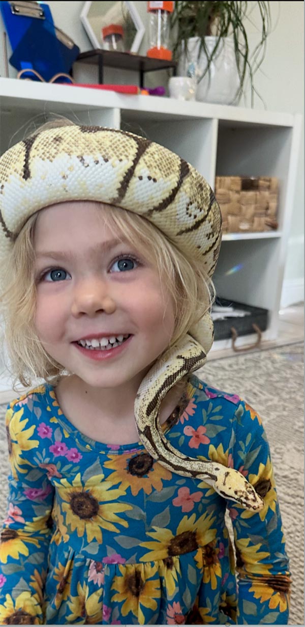 Pre-school-aged child with a snake wrapped around her head like a crown.
