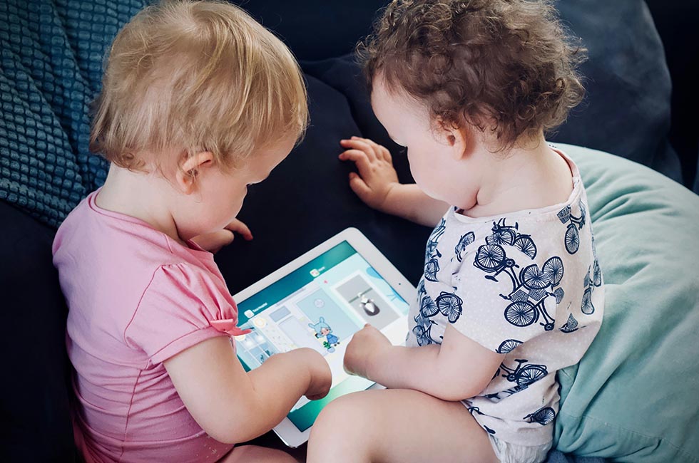 Two toddlers playing a game together on a tablet.