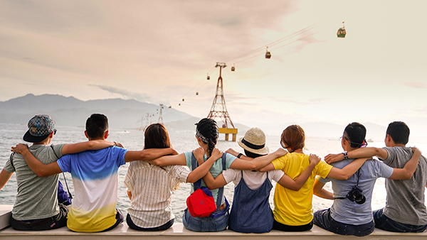 8 friends sit on a low wall overlooking the bay. They have their arms around each other's shoulders.