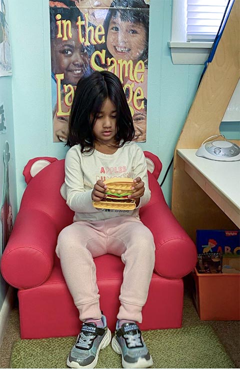 Young girl seated in a red chair reading a book.