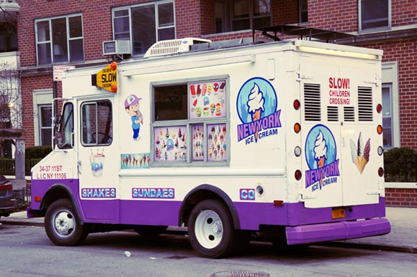 An ice cream truck with purple trim and signage sits at a New York city curb.