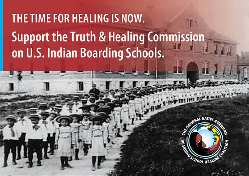 Archival black-and-white image of at least 100 Native American children lined up in rows down the dirt path. They school uniforms. Text at the top of the image reads, The time for healing is now. Support the Truth & Healing Commission on U.S. Indian Boarding Schools.