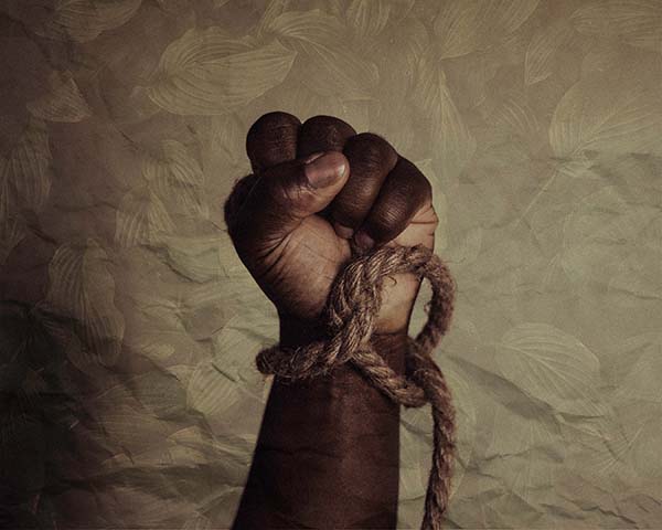 Closeup of a black man's fist with a rope loose around the wrist, as if it's just been untied