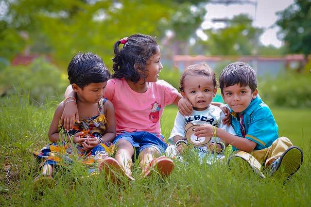 4 young children sitting in long grass with their arms around each other.