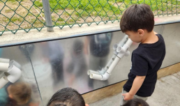 A preschool-aged boy inspects a plastic pipe attached to a metal wall