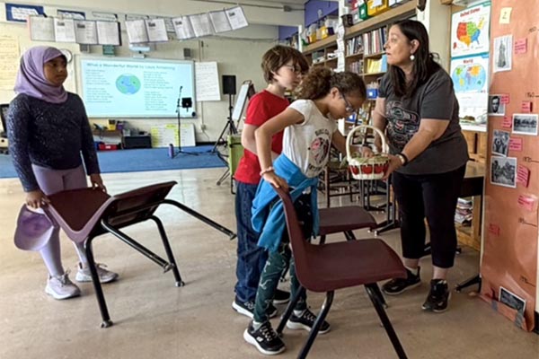 Kim Moberg offers memory stones in a wicker basket to 3 children in a classroom.