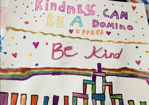 Close-up of a colorful poster with stacks of dominos, which reads, "Kindness can be a domino effect. Be kind."