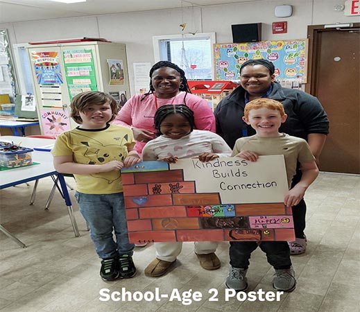 Three school-aged children and 2 teachers pose with thier poster Kindness Builds Connection. The poster features a brick wall.