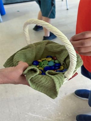 A wicker basket with a green towel and memory stones inside being offered to a young child.
