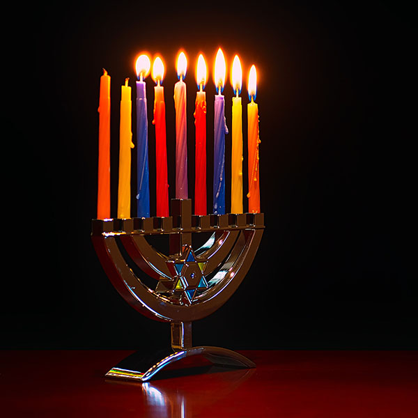 A menorah with 7 colored candles light against a dark background